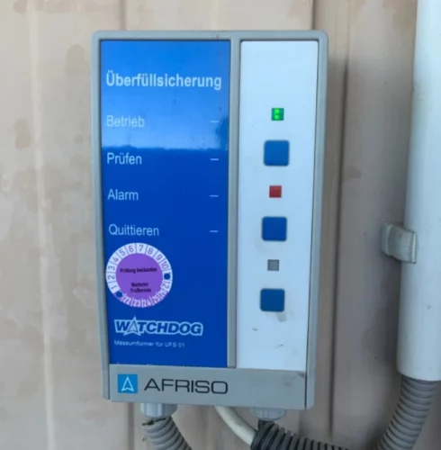 Kontrolleinheit einer Überfüllsicherung mit Prüfplakette.